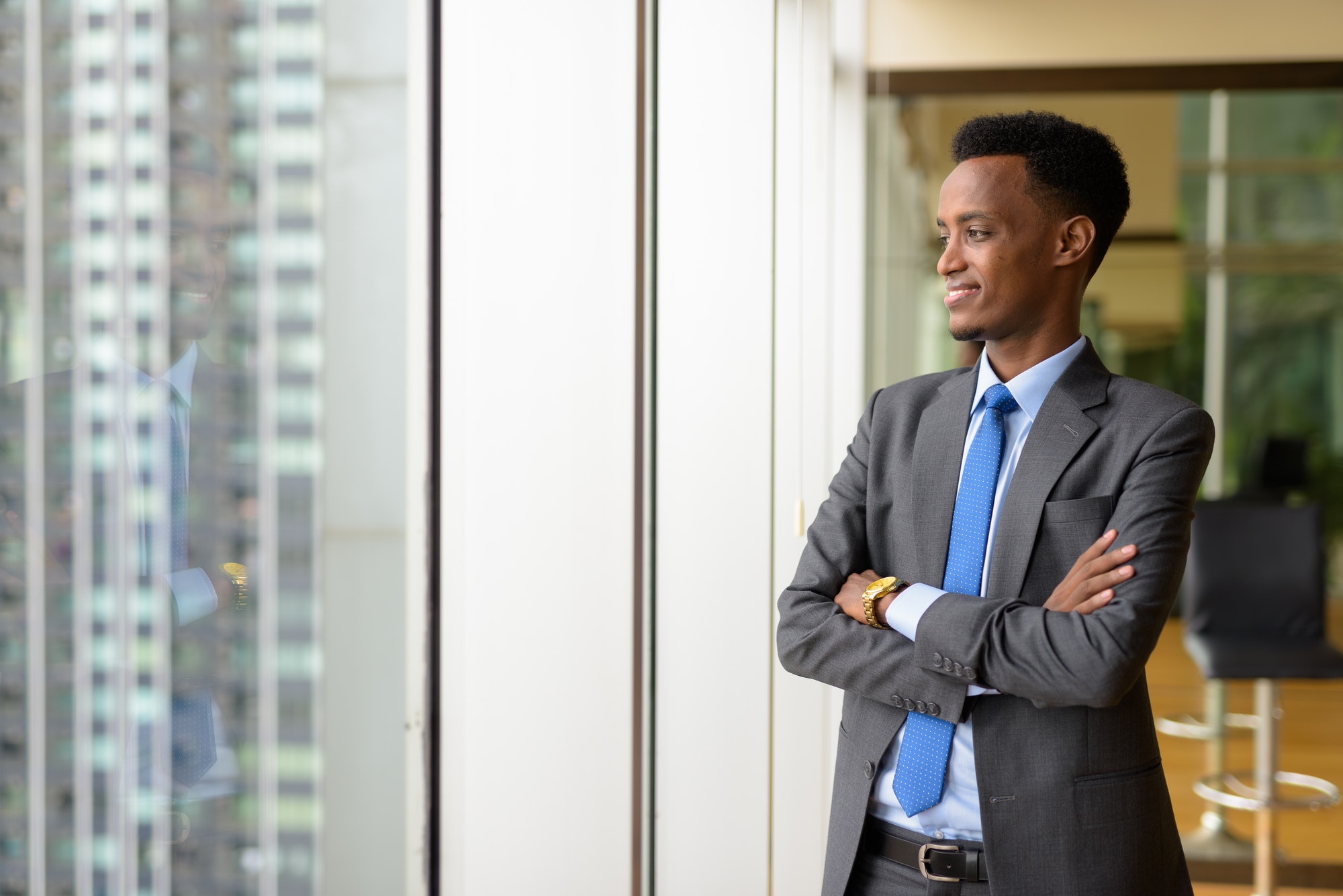 Portrait of handsome African businessman looking through window while thinking